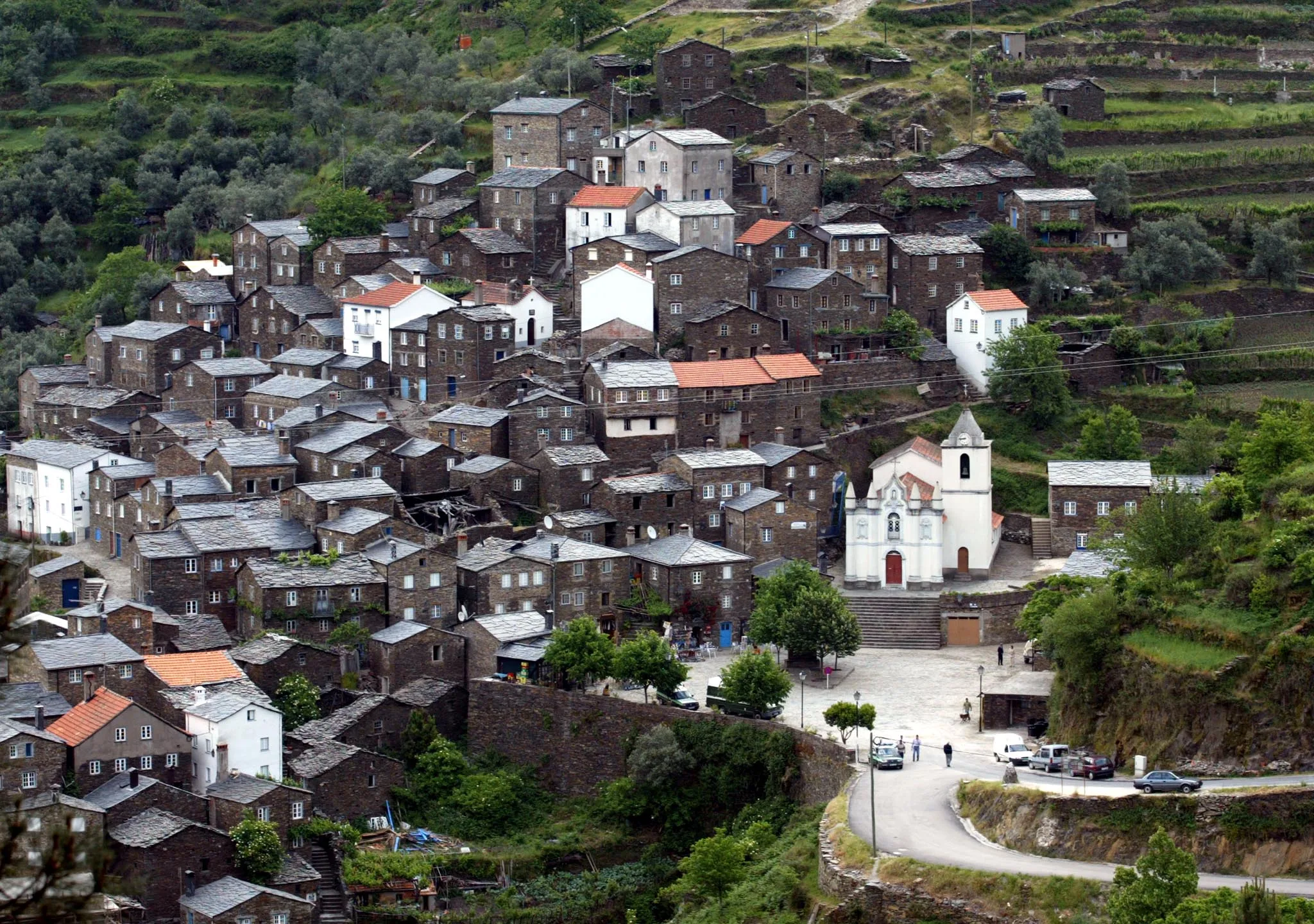 Vista panorâmica da aldeia histórica de Piódão, em Portugal, com casas de xisto agrupadas na encosta e igreja branca em destaque na praça central.